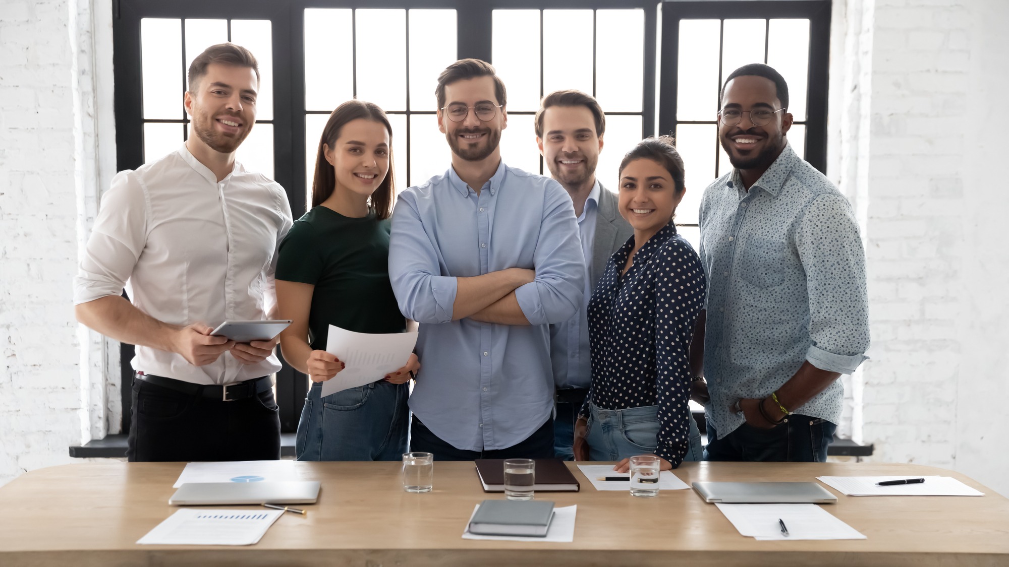 Corporate Photo Smiling Diverse Employees With Confident Executive Wearing Glasses Standing in Modern Office Room, Looking At Camera, Successful Startup Founder With Team, Staff Members.